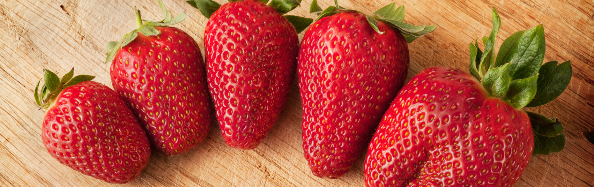 Five strawberries of various sizes and shapes are arranged on a brown table.