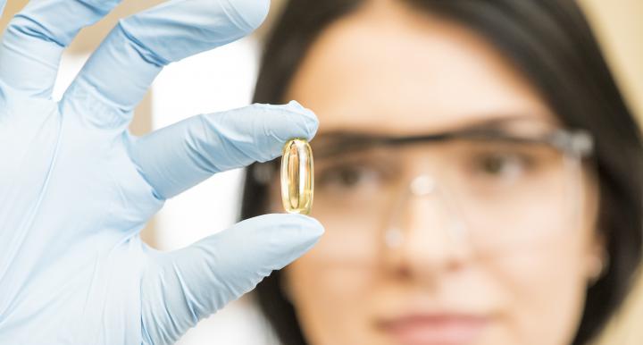 Female scientist examining omega-3 capsule.